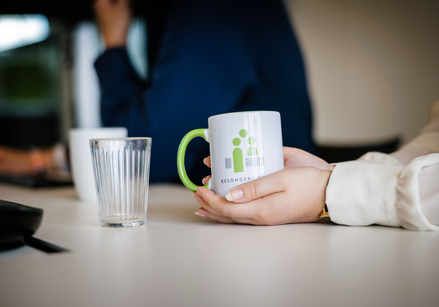 One hand holds a white cup with a green logo on it
