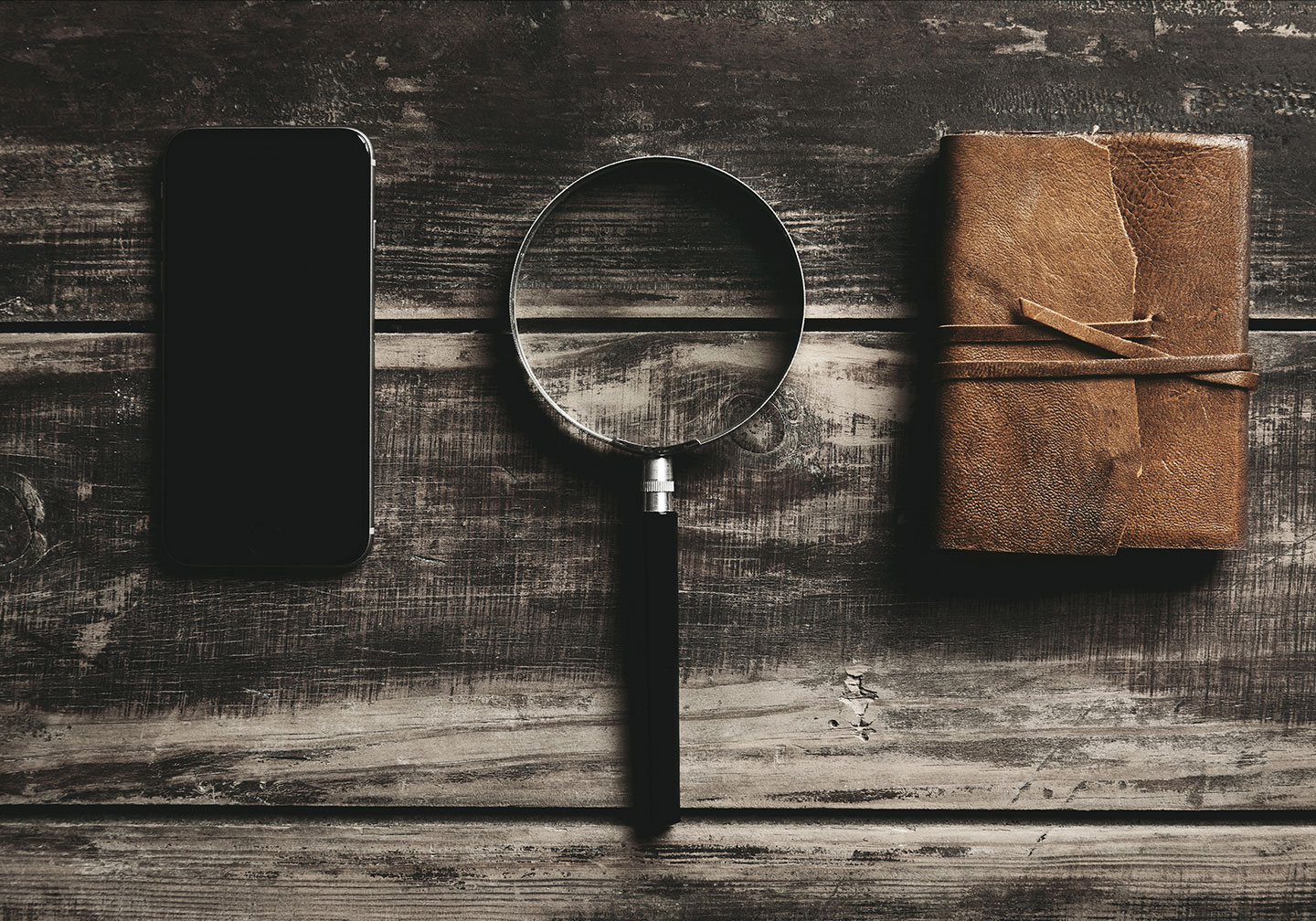 A smartphone, a magnifying glass and a notebook lying on a wooden table