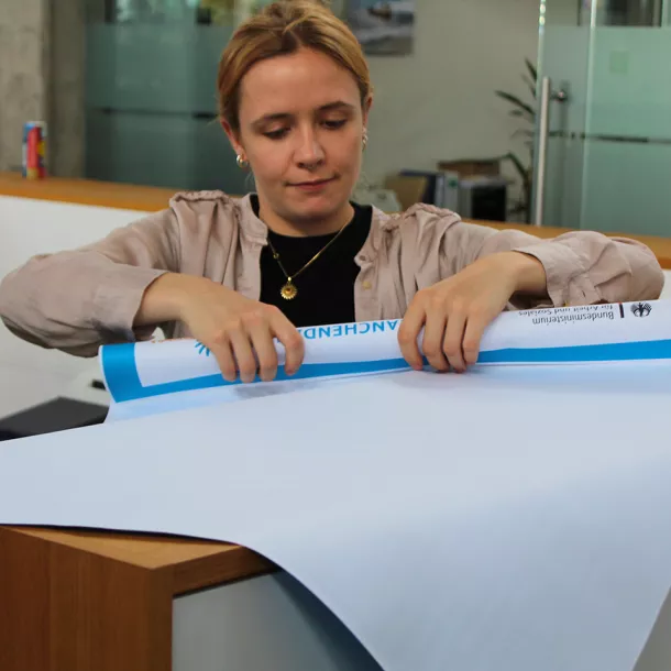 Eine Mitarbeiterin rollt ein blaues Plakat auf