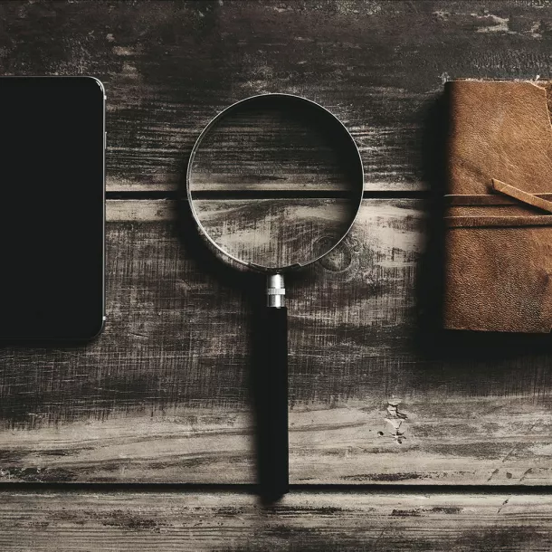 A smartphone, a magnifying glass and a notebook lying on a wooden table