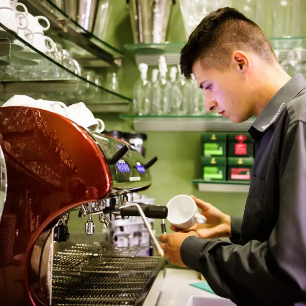 Kellner bereitet Milchschaum an Kaffeemaschine zu