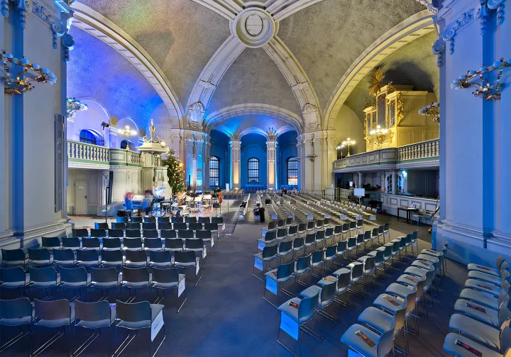 Blue-lit church hall with many rows of chairs and an organ on the left
